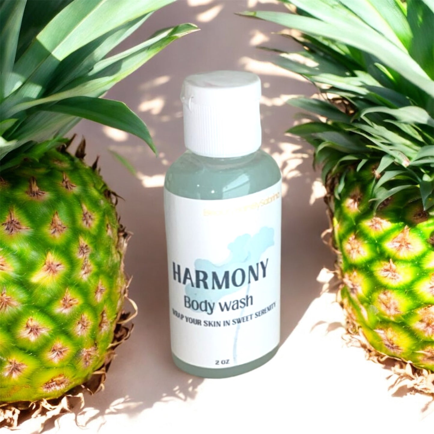 Harmony body wash bottle between two pineapples on a neutral background