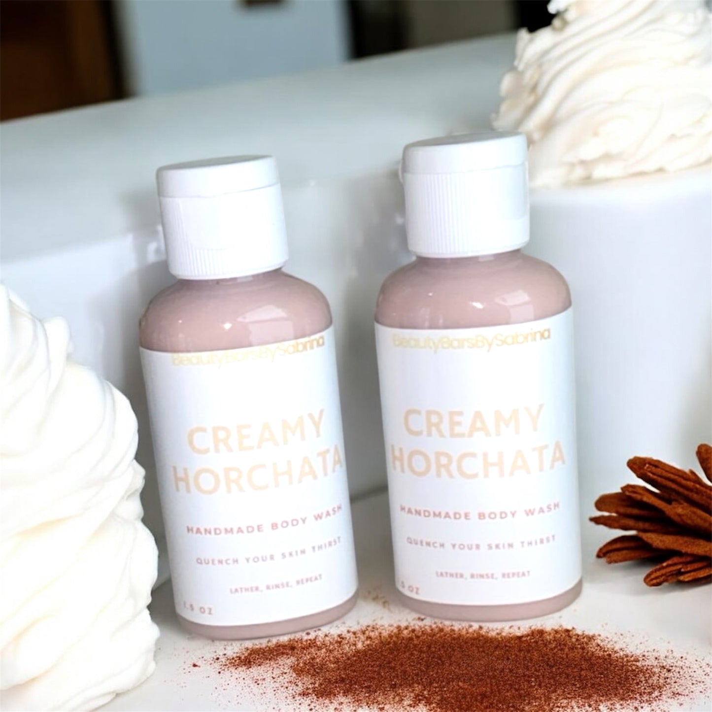 Two bottles of 'Creamy Horchata' body wash on a surface with cinnamon sticks and a decorative item.