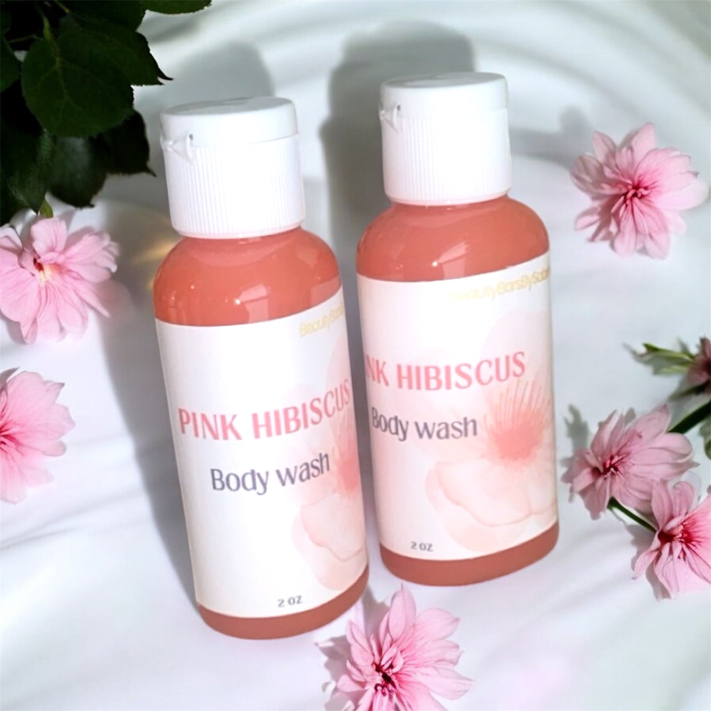 Two bottles of Pink Hibiscus body wash with pink flowers around them on a white background.