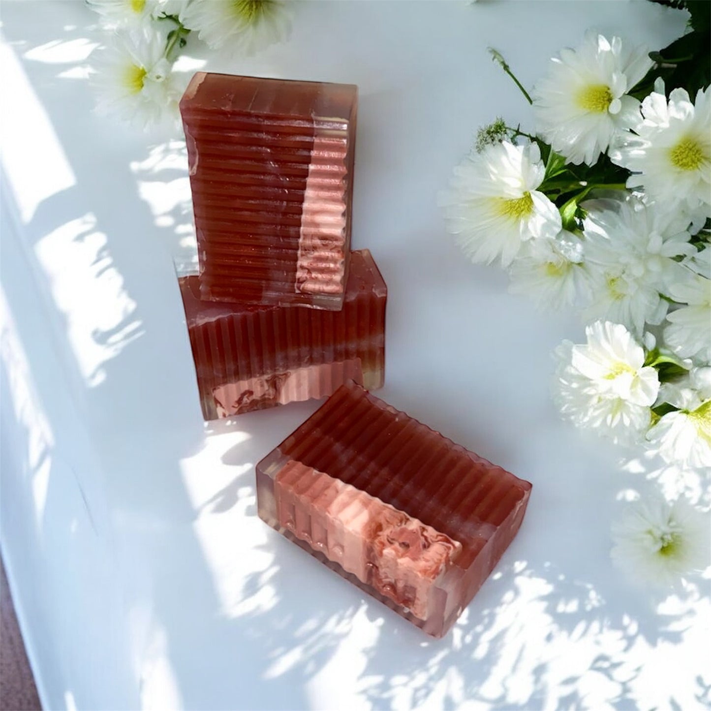 Three rectangular soap bars with a marbled pattern on a white surface with white flowers.