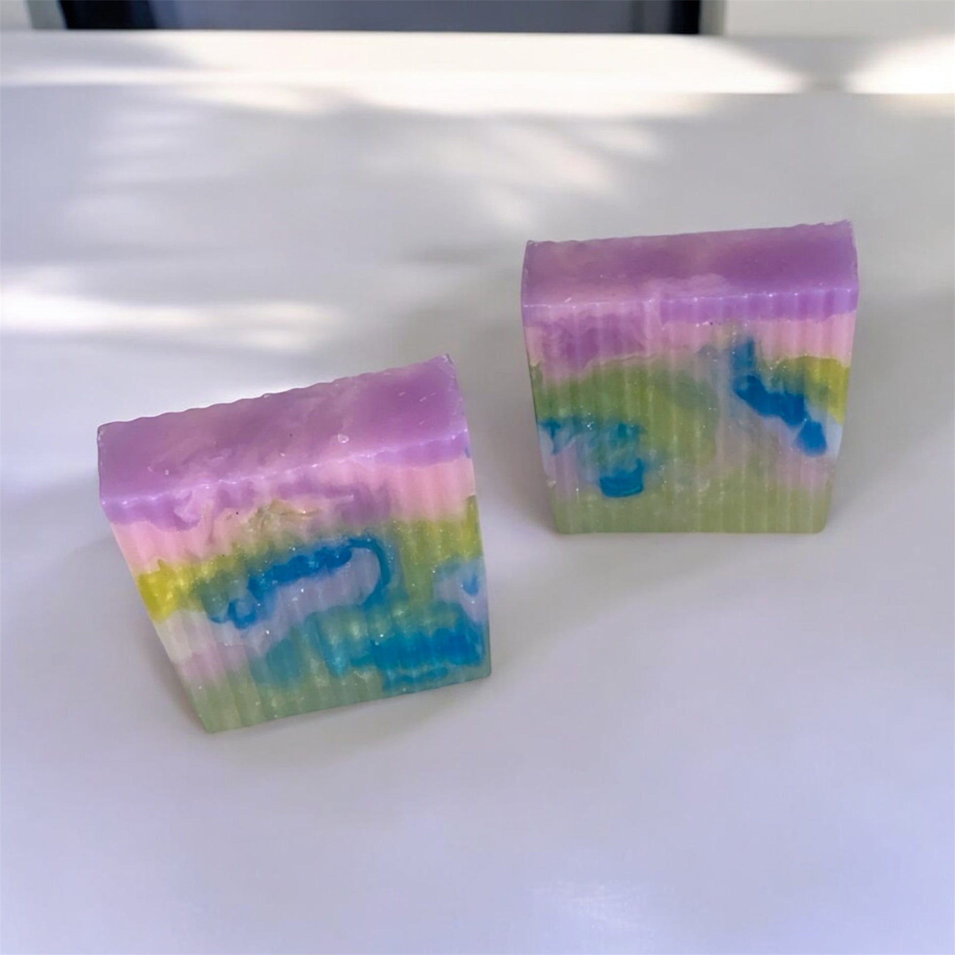 Two colorful soap bars with a rainbow pattern on a white surface.