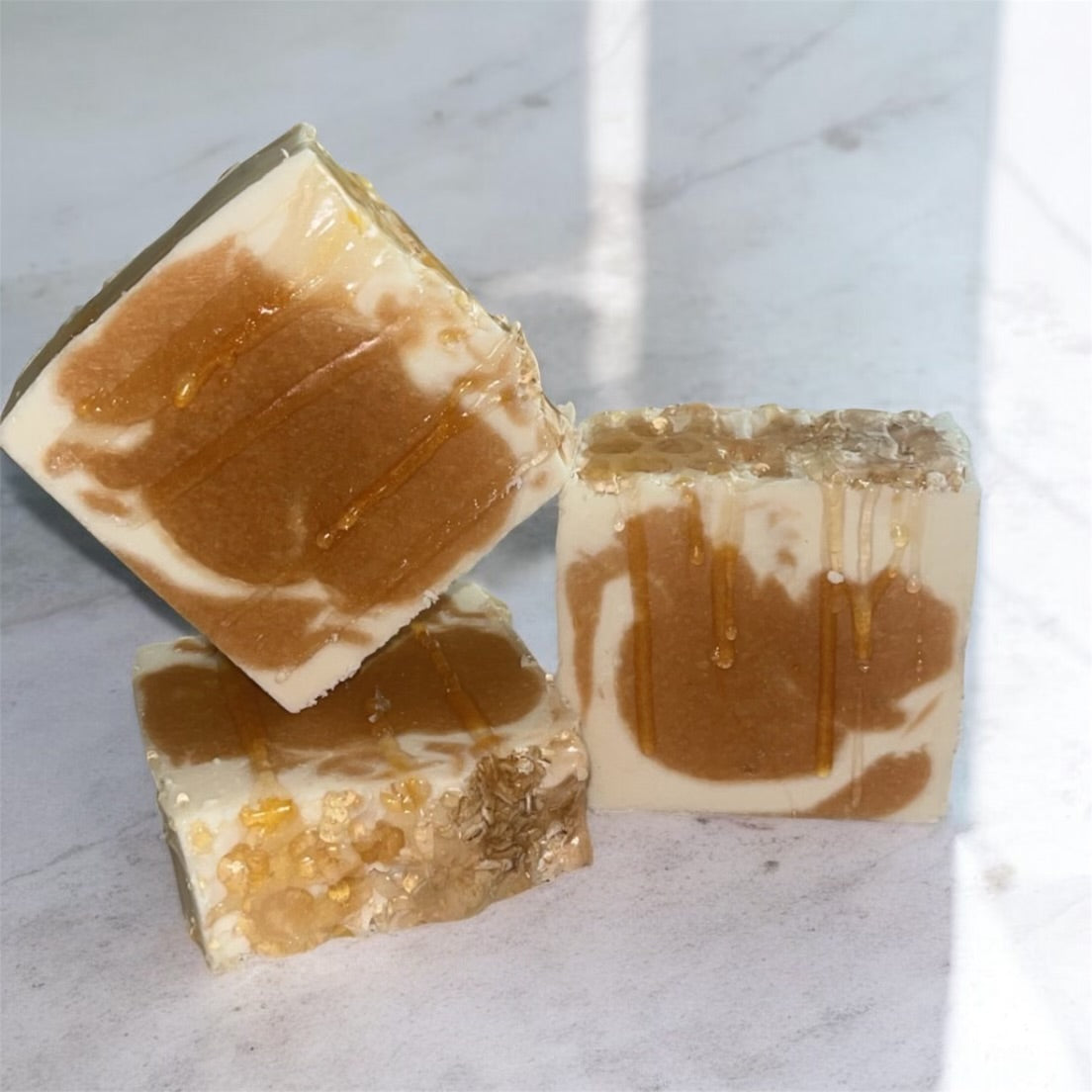 Three pieces of brown and white marbled soap on a light gray surface