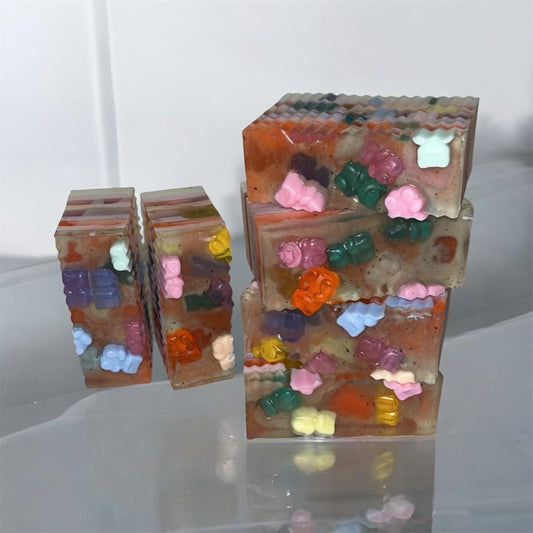 Stack of colorful gummy bear-shaped soap bars on a reflective surface.