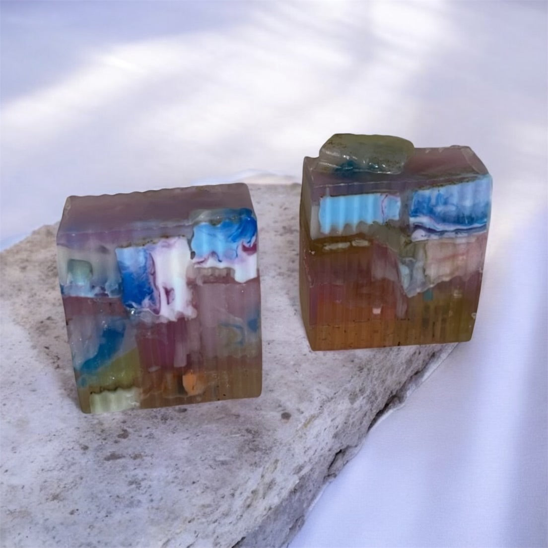 Two rectangular soap pieces with embedded colorful designs on a textured surface.