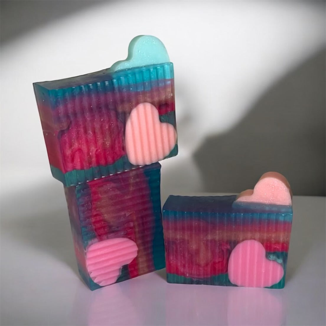 Stack of colorful soap bars with heart shapes on a reflective surface
