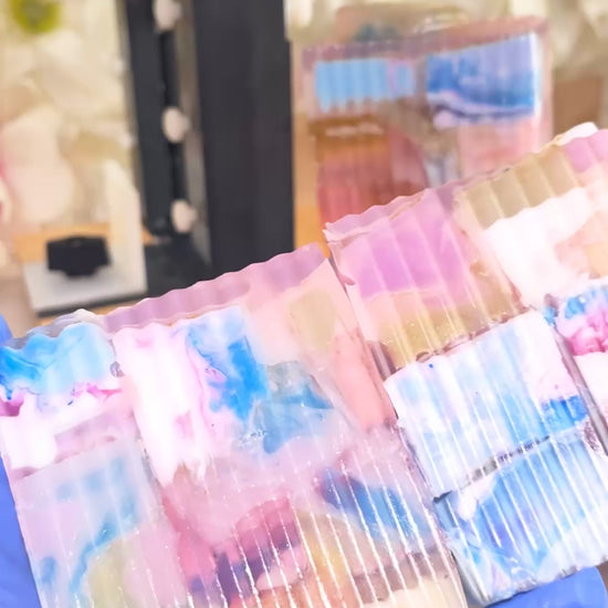 2 colorful soaps being held with blue gloves and being turned around with soap in background 