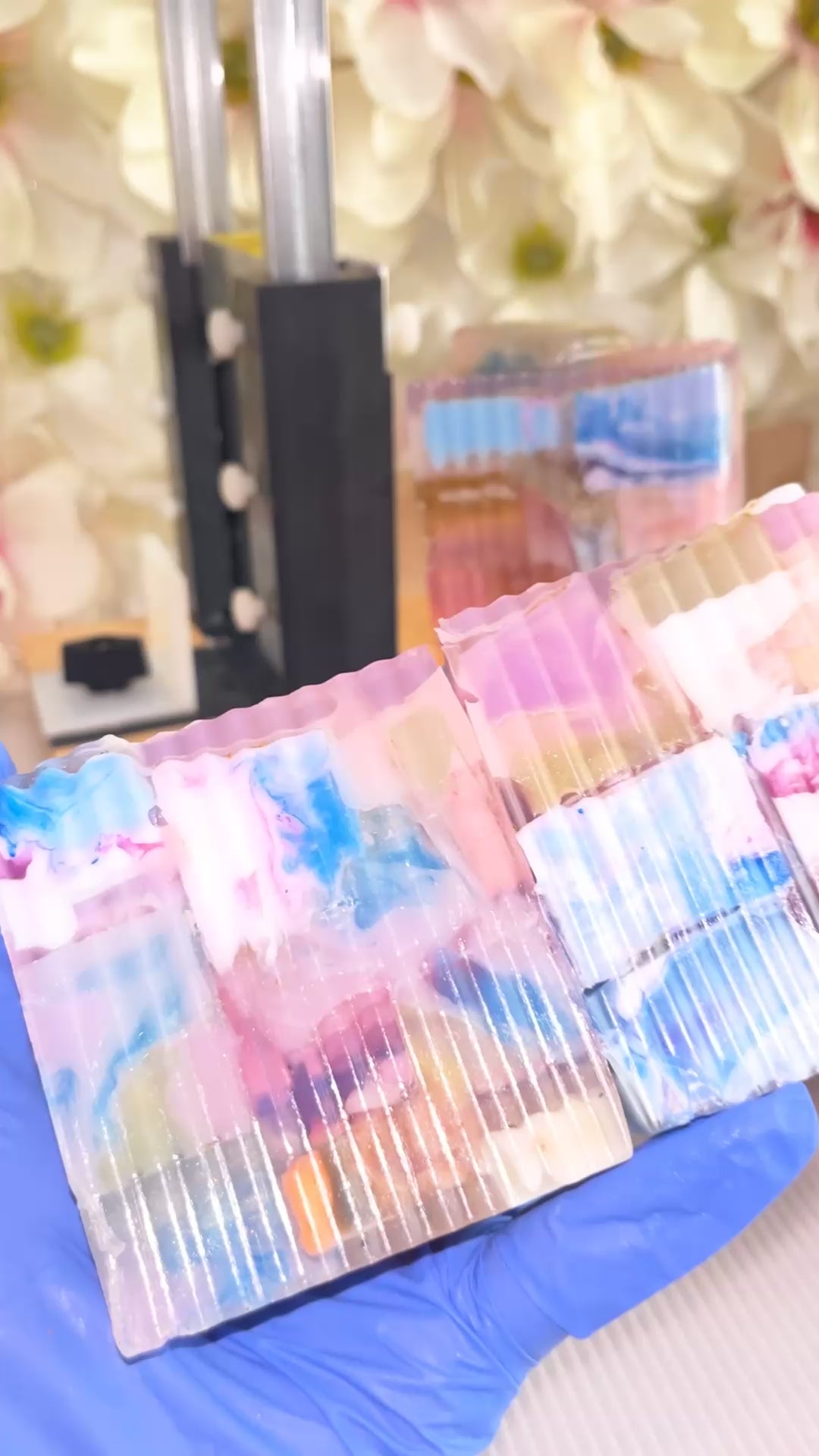 2 colorful soaps being held with blue gloves and being turned around with soap in background 