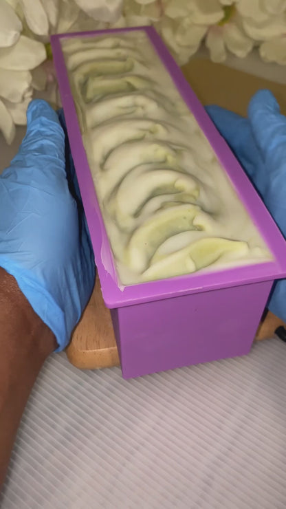 Video showing holding a green and white soap in a mold with blue gloves on