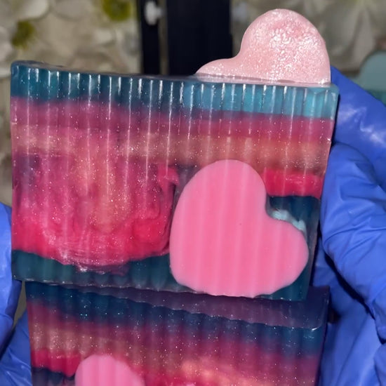 Hand with blue gloves holding 2 colorful pink and Purple Heart embed soaps.