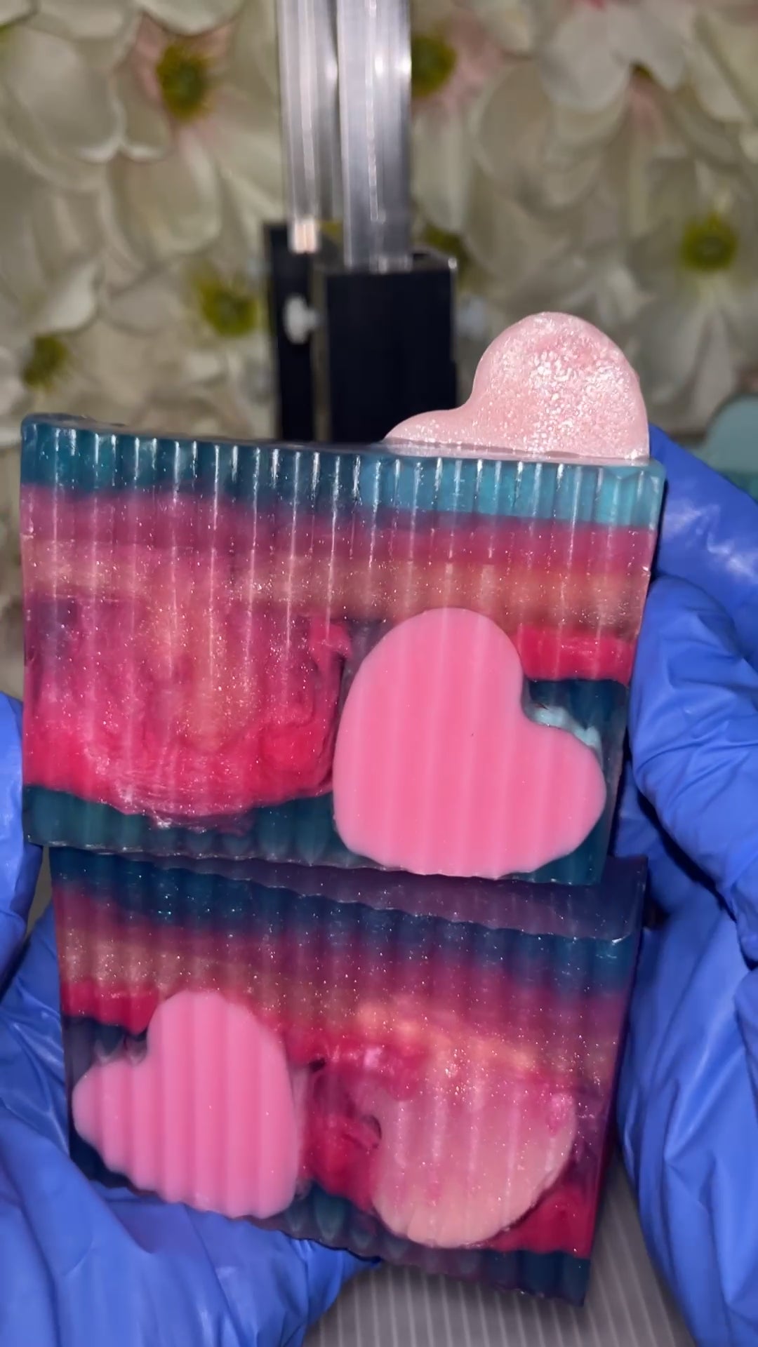 Hand with blue gloves holding 2 colorful pink and Purple Heart embed soaps.